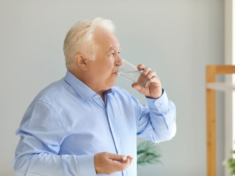 Mężczyzna w sile wieku popija wodą tabletkę kwasami Omega-3.